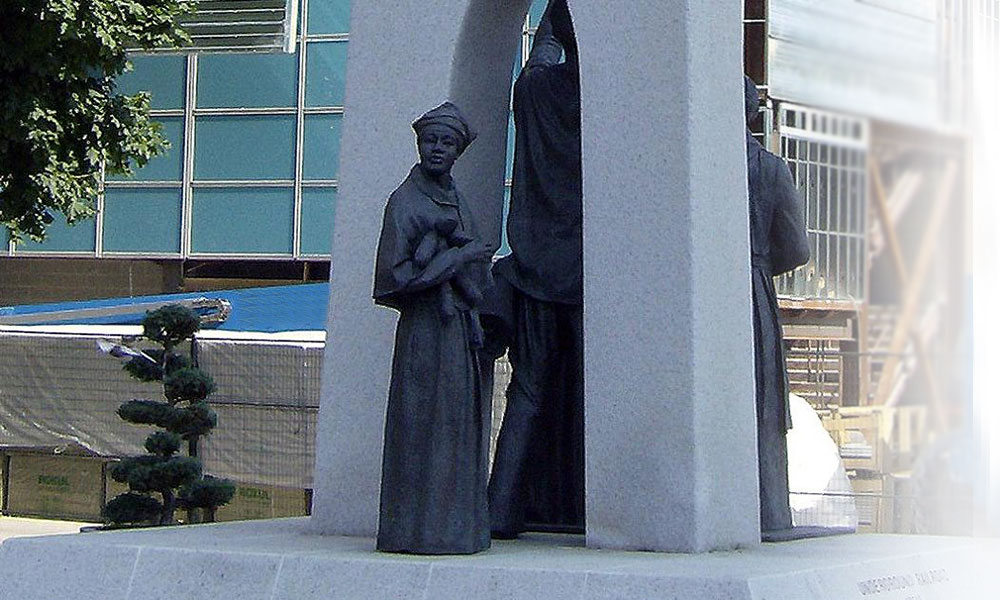 Statue de bronze d'une femme noire tenant un bébé et franchissant le seuil d'une porte en ciment